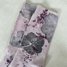 Botanical Geranium Socks - Melo Handmades. Pair of lavender-toned socks with botanical dye patterns, worn on a bed with soft white linen.