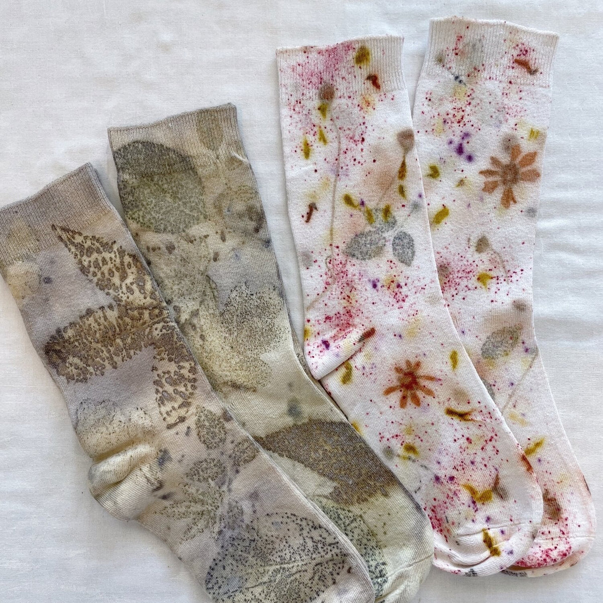 Botanical Eucalypt Socks - Melo Handmades - Two pairs of botanical-dyed socks laid flat on white linen: one in earthy eucalyptus tones of green and brown, the other with a speckled floral pattern in pink, gold, and rust