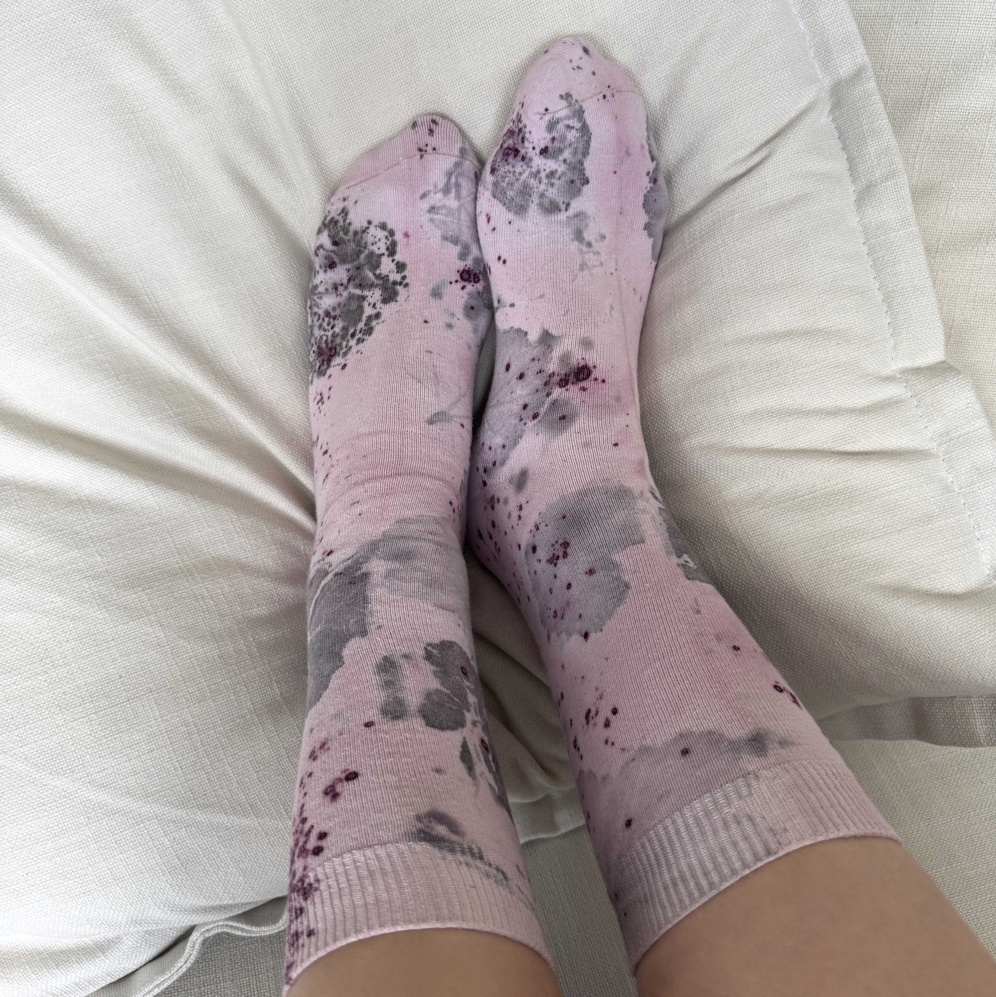 Botanical Geranium Socks - Melo Handmades. Pair of lavender-toned socks with botanical dye patterns, worn on a bed with soft white linen.